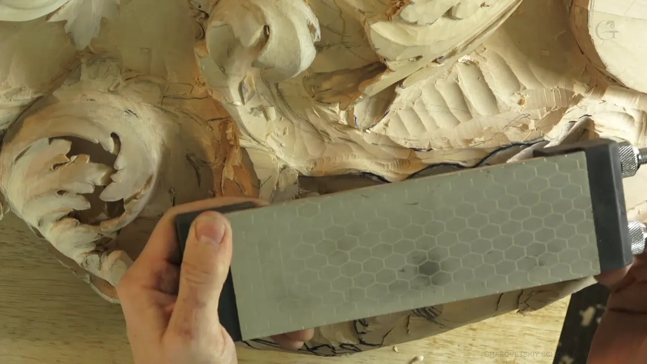 Diamond stone with its honeycomb bond pattern, held flat over a half carved acanthus panel on the workshop bench
