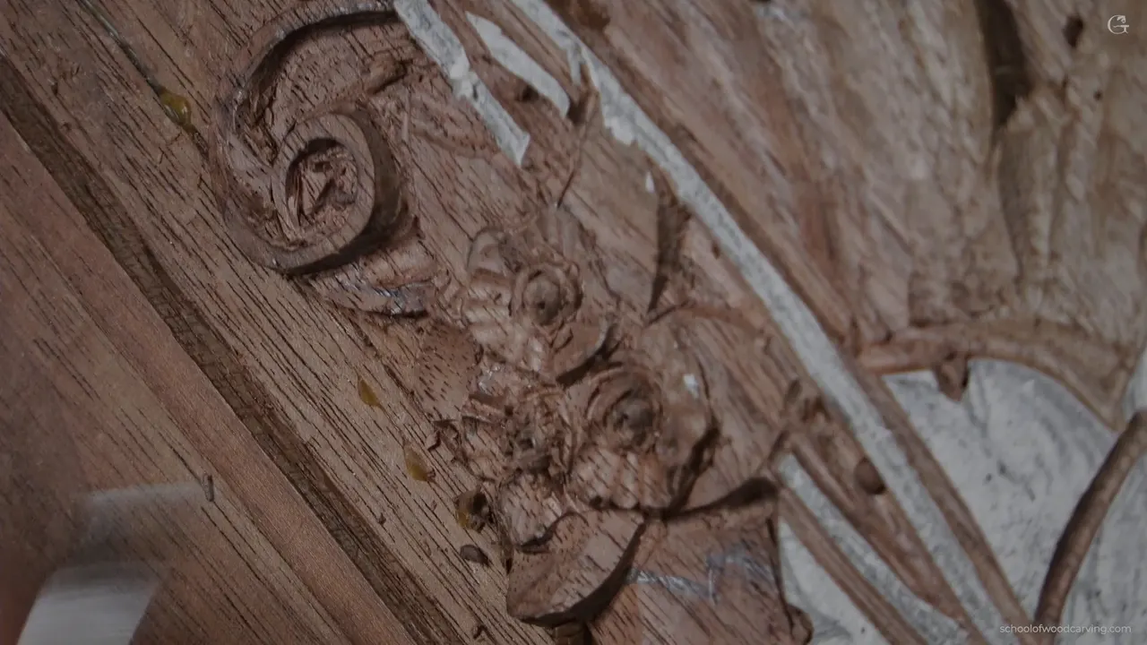 Small carved flowers with a scroll running past them, cut shallow in walnut.