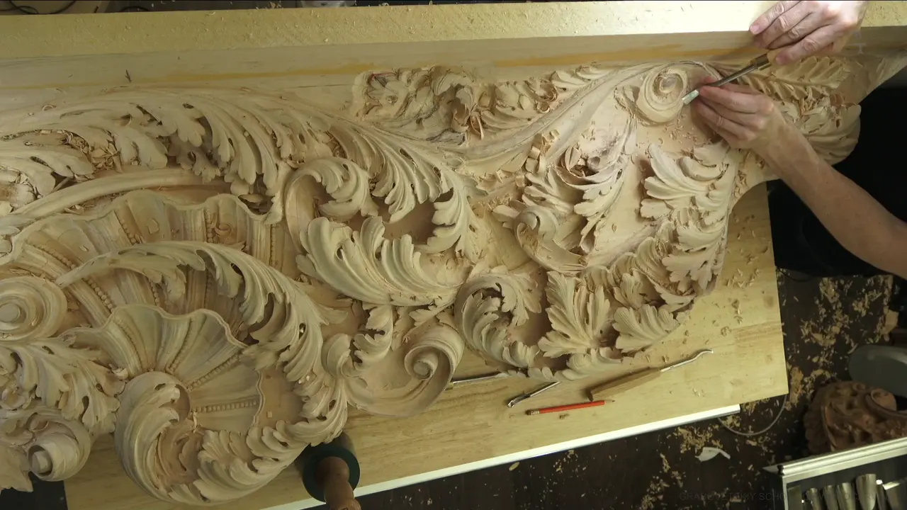 The whole carved panel from above, two arms working at the top right, a red pencil on the bench.