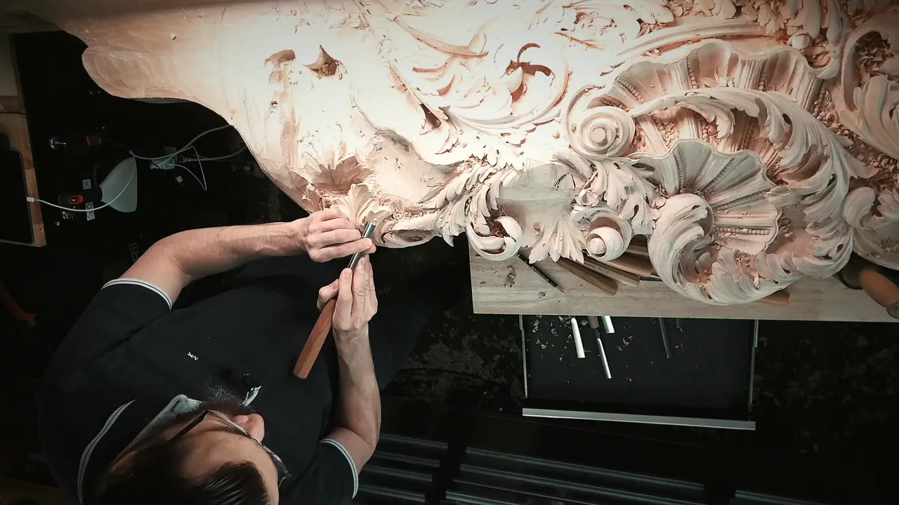 Alexander Grabovetskiy in glasses reaching up with a red handled gouge into the panel above him
