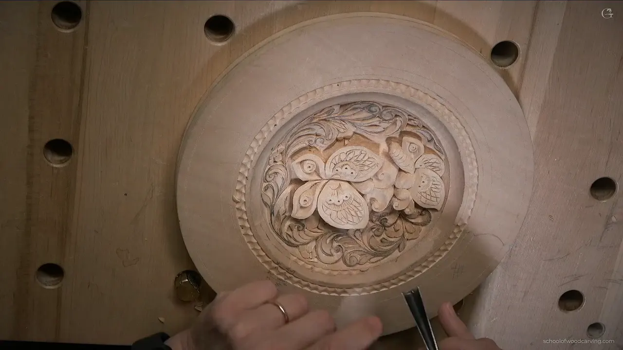 A hand brings a gouge to the lower rim, a finished ring of cuts around the dish