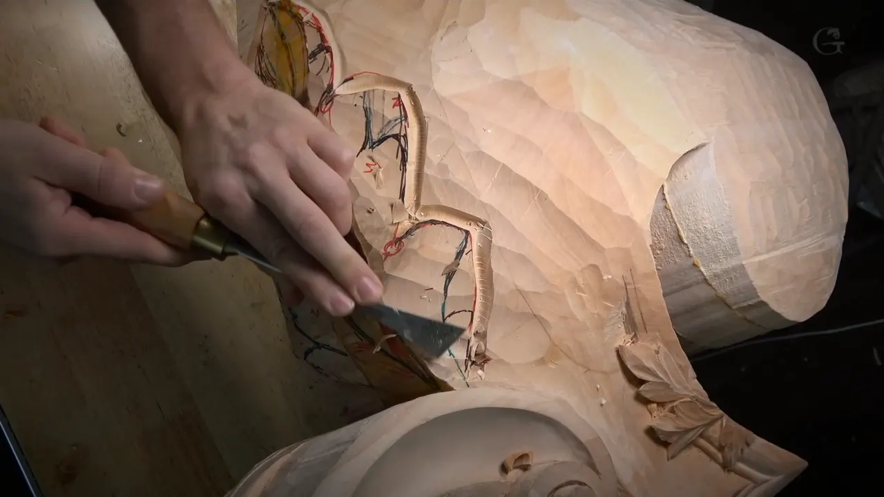 Two hands guide a skew chisel along the outline of an acanthus leaf marked in red and blue