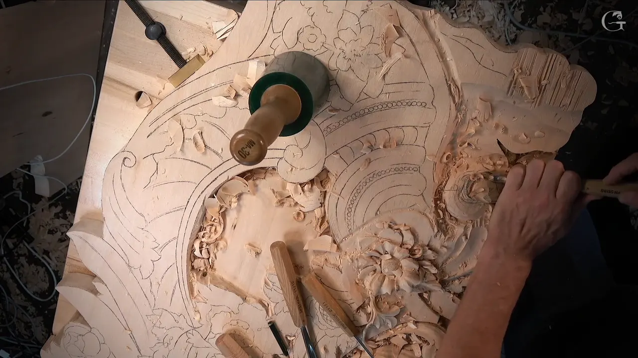 Whole panel seen from above, a mallet standing on the drawing, gouges lying below and one hand carving at the right