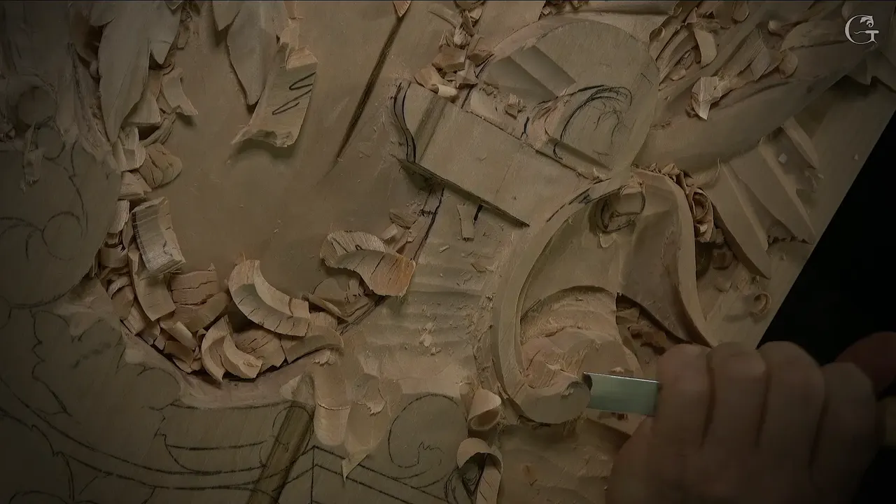 Close up, a flat gouge pushed across the lowered area beside the volute, chips piled on both sides