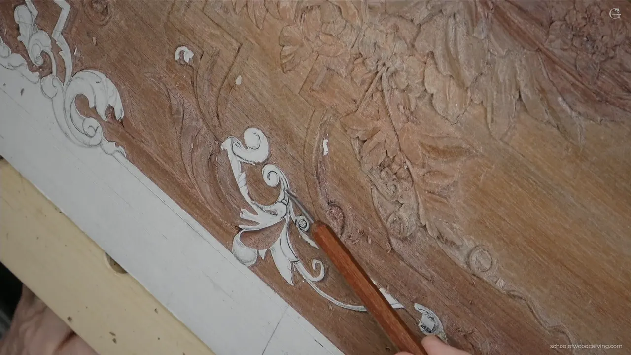 A gouge lying across the carved scrollwork of the panel, handle toward the camera.