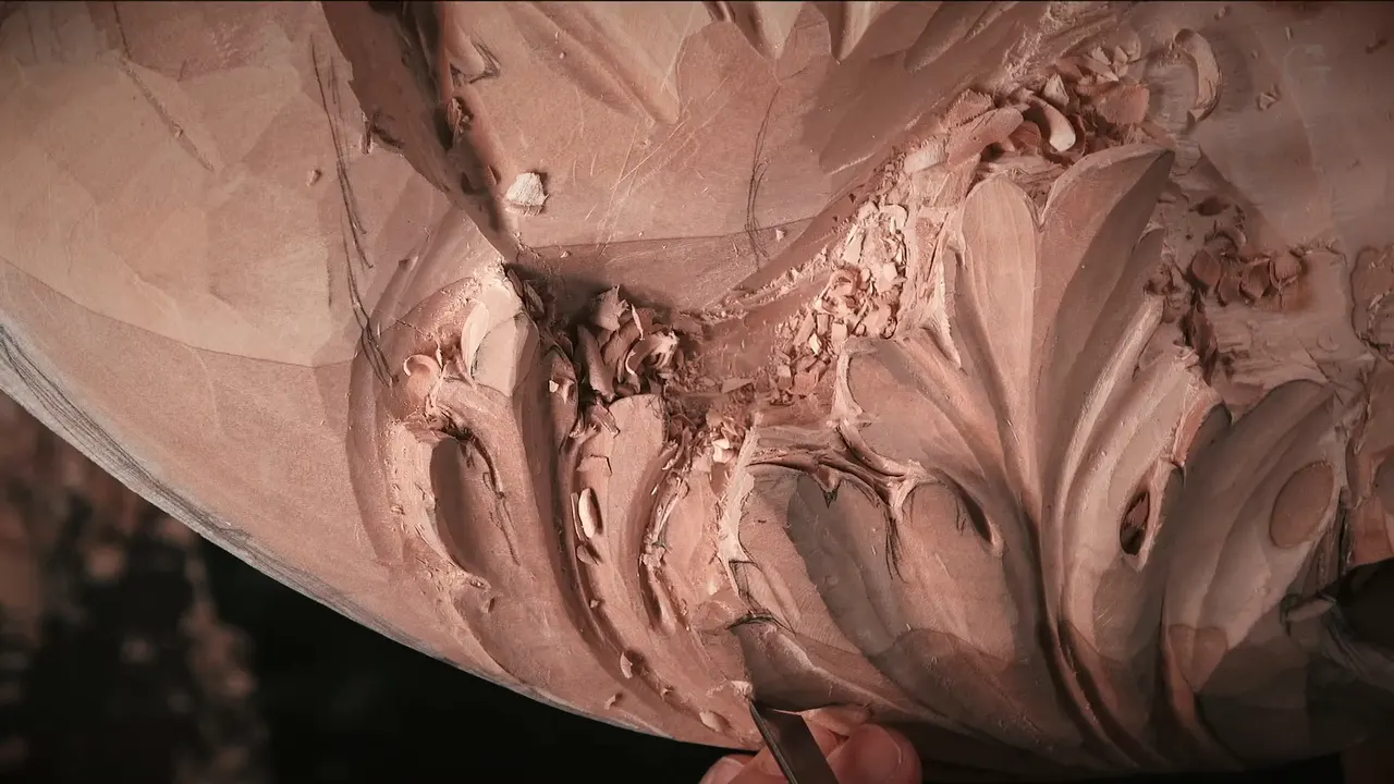 Dark handle and a gouge tip working between two carved lobes, fresh chips heaped above