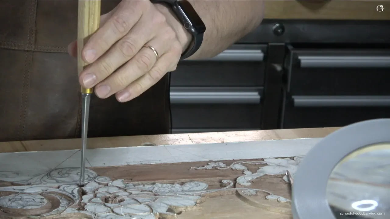 A gouge stood straight down in the carving, a wedding ring and a watch on the hand that holds it
