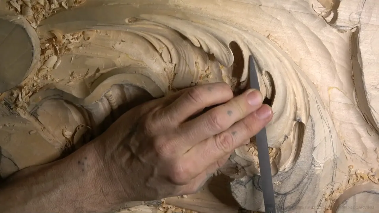 A flat grey rasp held against the curl of a carved acanthus leaf, chips all around.