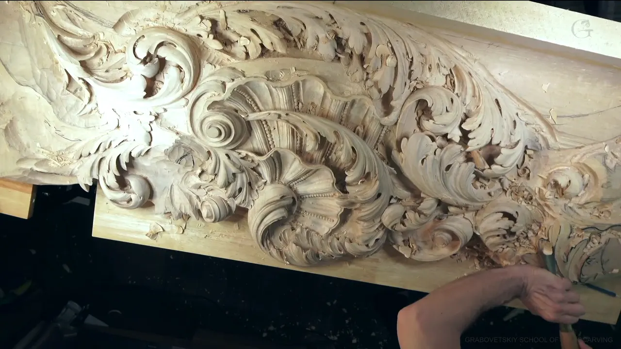 The whole carved board from above, shell and scrolls at the left, my hands working at the far right.