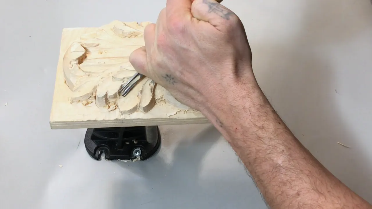Right arm reaching across the basswood panel, gouge down in the lower left of the carved leaf