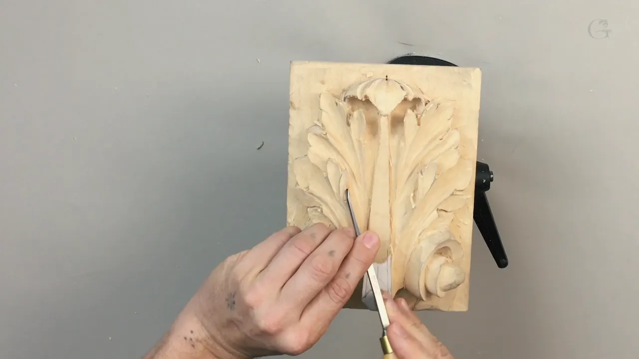 Small panel held upright while both hands drive a white handled gouge into the middle of the leaf