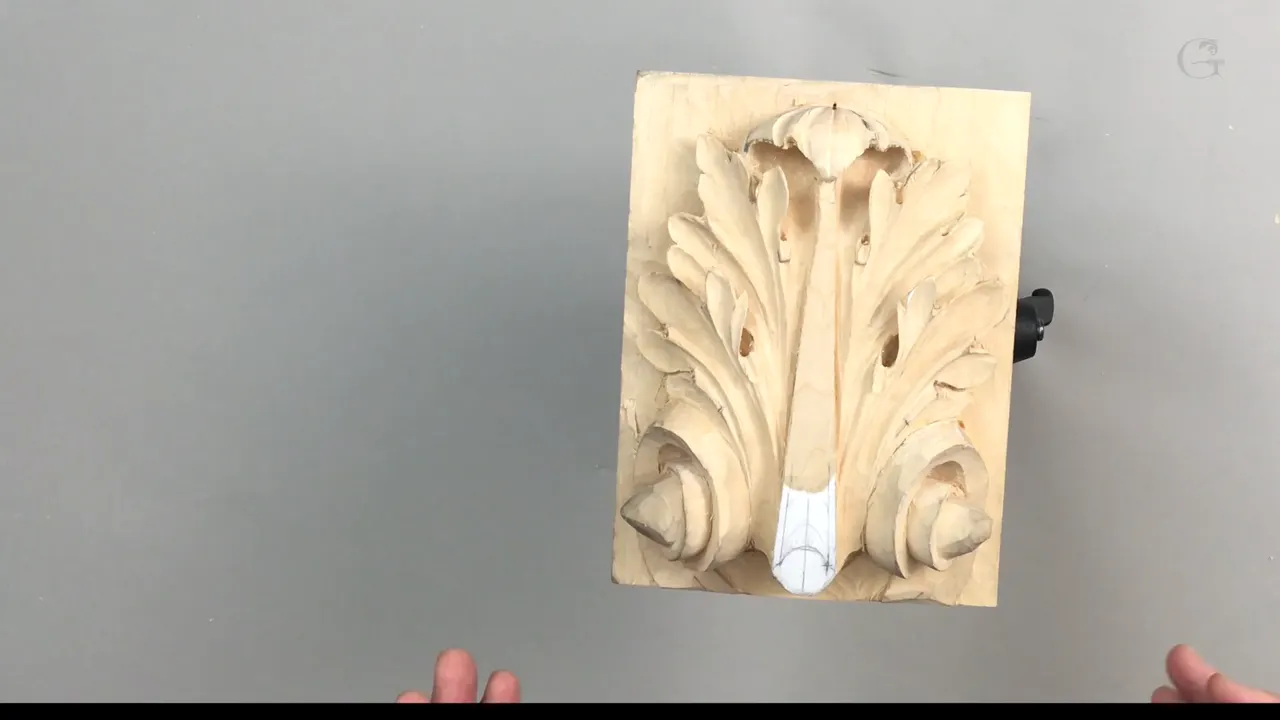 Carved leaf standing alone in the vise, half its detail still waiting, nobody's hands anywhere near it