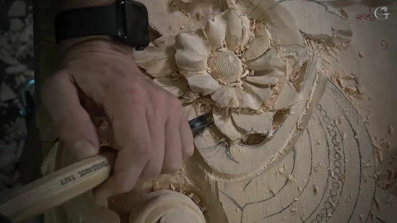 Hand on a stamped gouge handle, its edge down in the hollow beside the flower