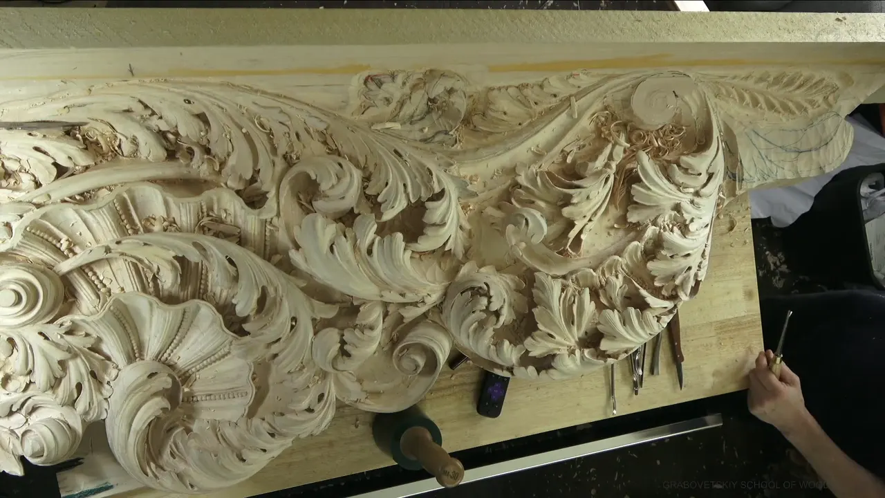 Whole carved panel seen from above at the end of workshop 61, tools and a mallet laid along the bench edge