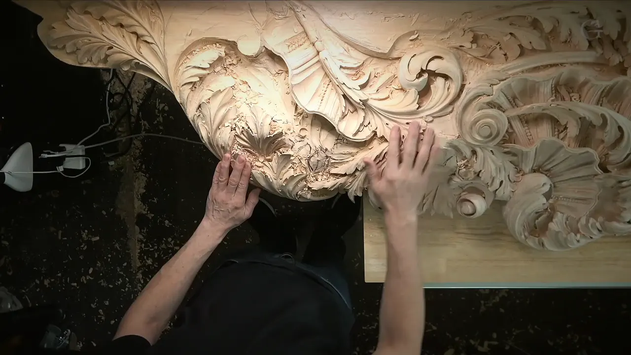 Both hands flat on the carved panel, scrolls and a shell along its edge