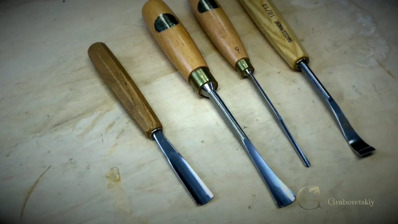 Five carving gouges laid out side by side on a pale board.