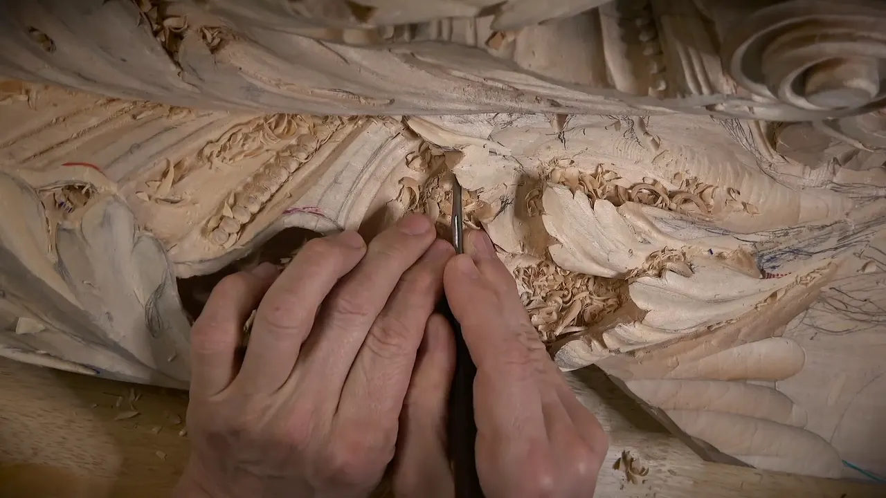 Two hands steady a small tool upright in a tight spot of the carving