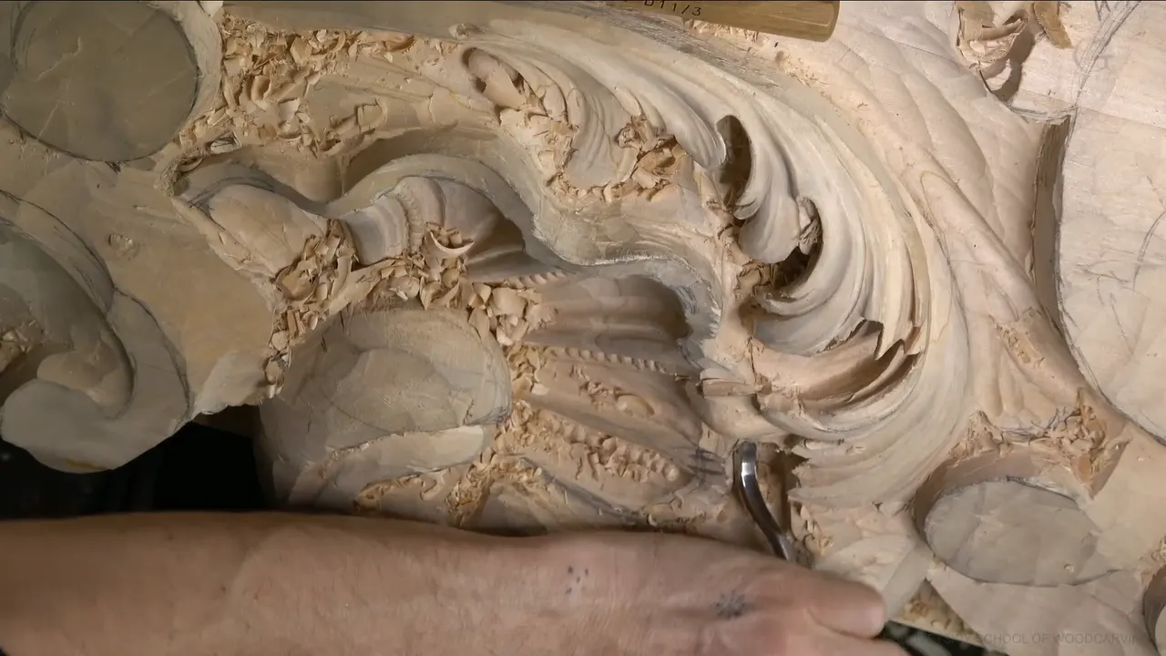 A bent spoon veiner reaching up under the edge of a carved acanthus lobe, one arm across the panel.