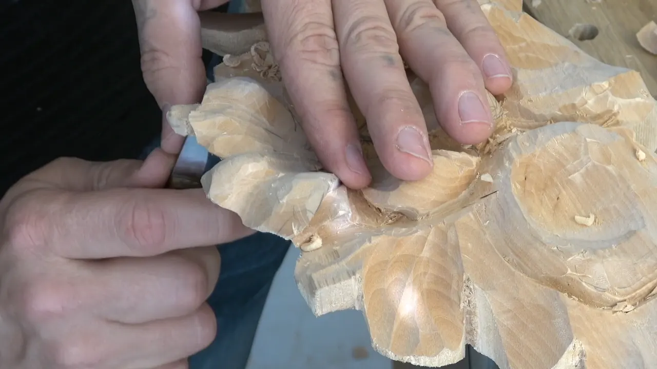 Both hands steadying the flower while a knife works along the outer edge of one petal