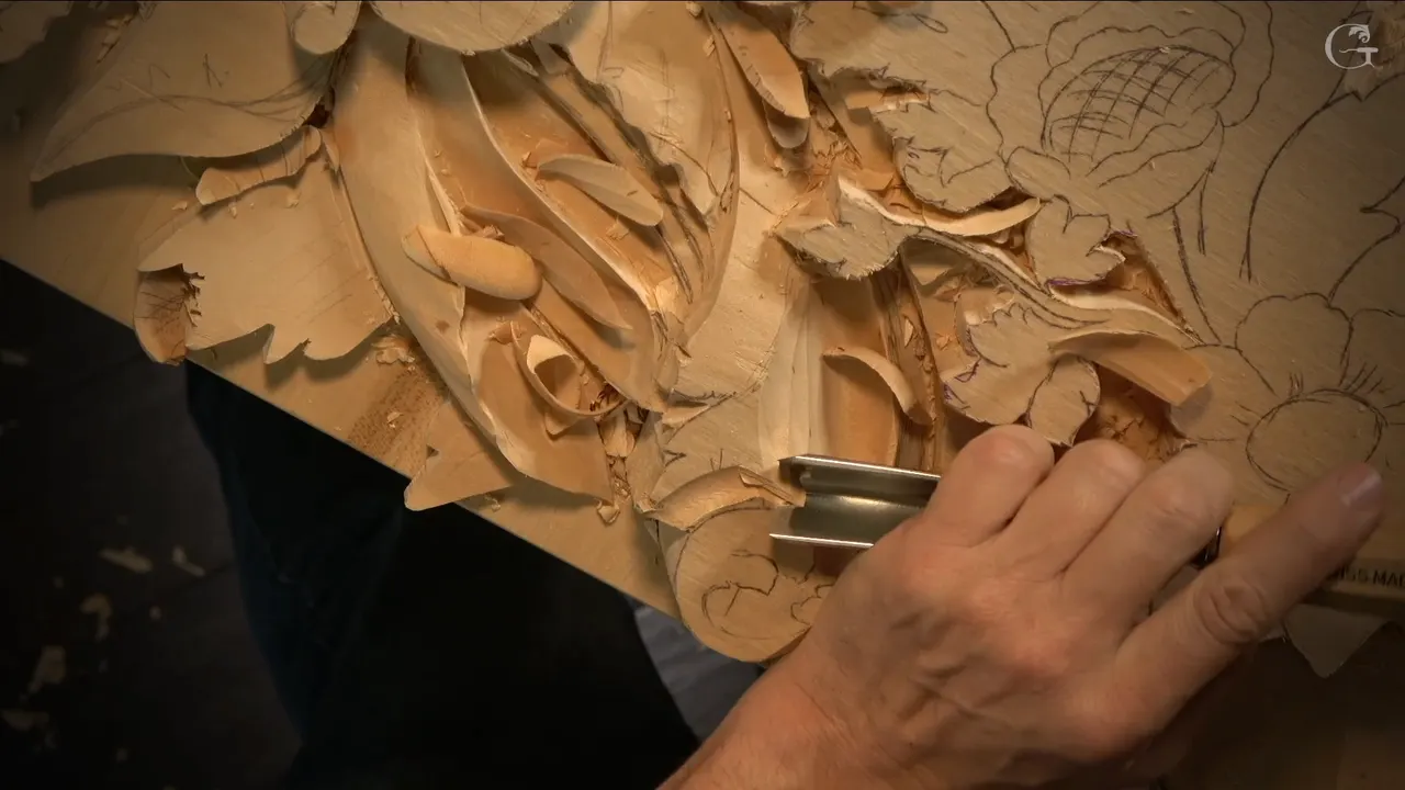 A wide U shaped gouge lies on its side under one hand beside the carved acanthus