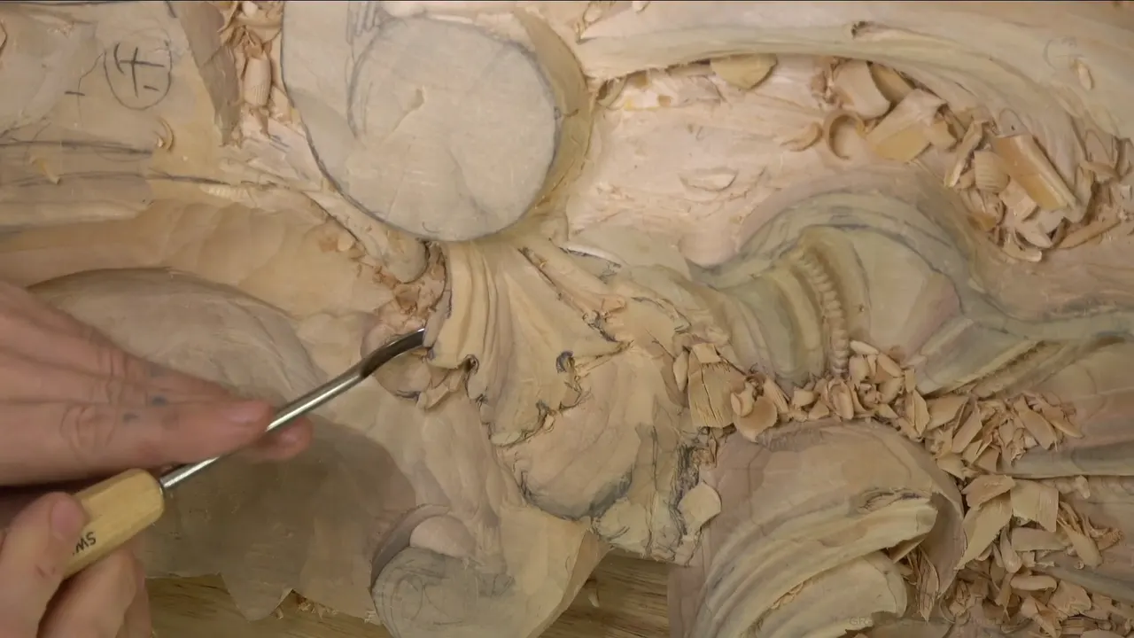 Slim bent tool under an acanthus fan, round disc above.