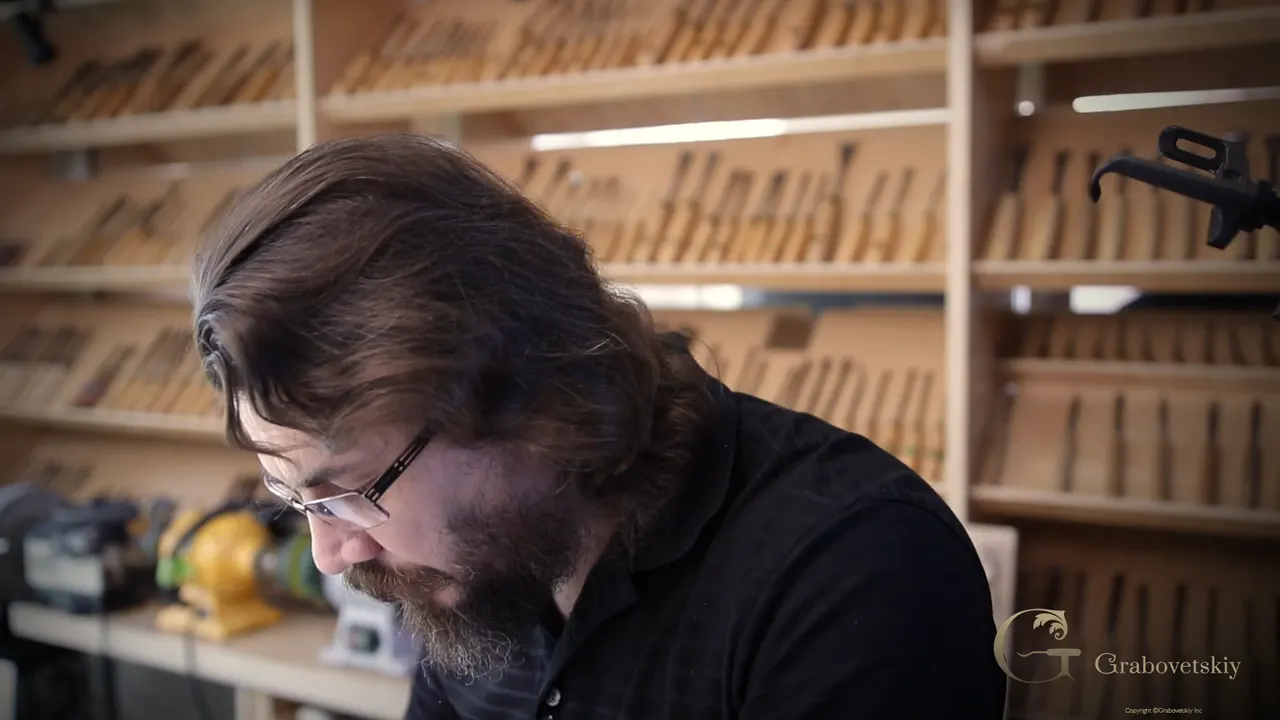 Alexander looking down at his bench, the rack of gouges and knives filling the wall behind him.