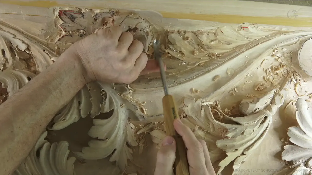 One hand braces the steel of a gouge while the other holds its yellow handle.