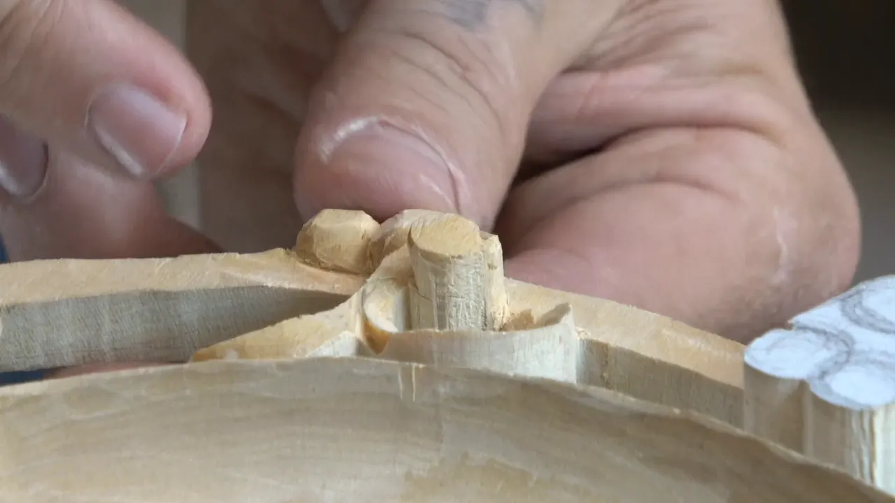 Fingertips steadying the panel while a small gouge works the pair of berries at the rim.