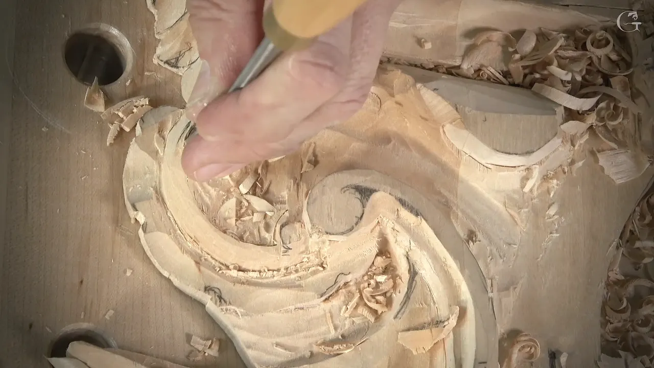 A yellow handled gouge in my fingers at the left curl of the scroll, with chips lying all around it