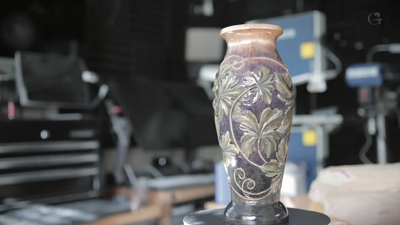 The finished vase stands upright, purple ground behind gray green leaves