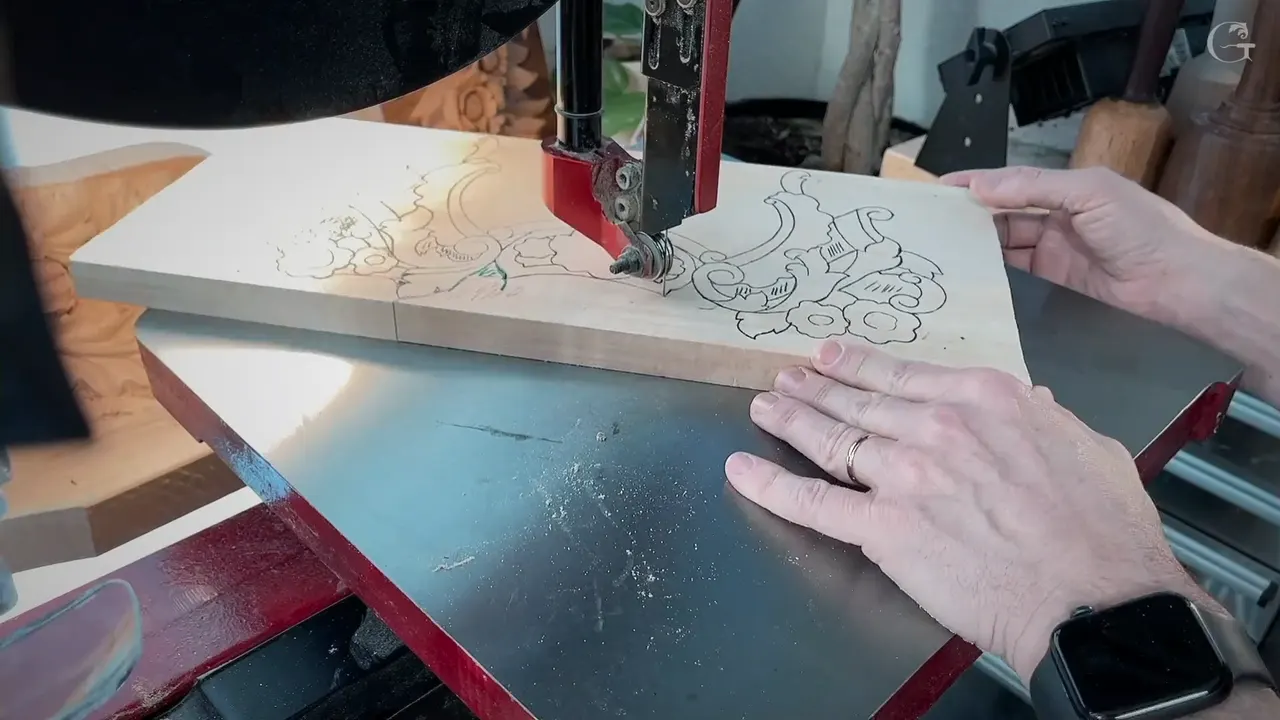 Two hands push a drawn board into a thin band saw blade, scrolls and flowers inked on the wood