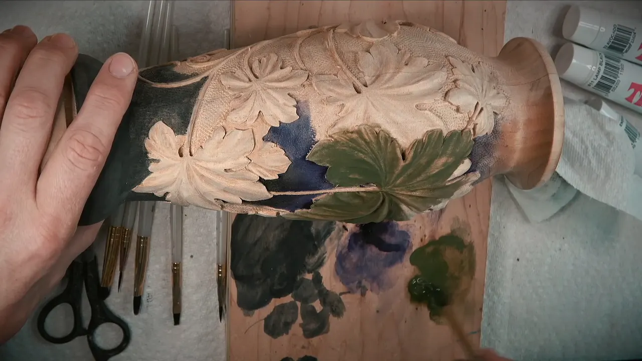 Carved vase on its side, black at the base, purple between the leaves and one leaf brushed green
