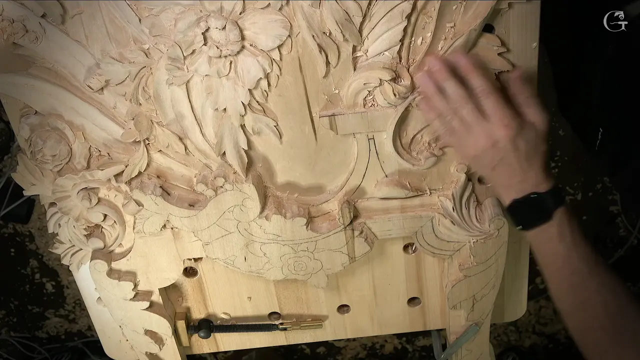 The whole panel seen from above, carved flowers and leaves along the top, a hand at the right edge