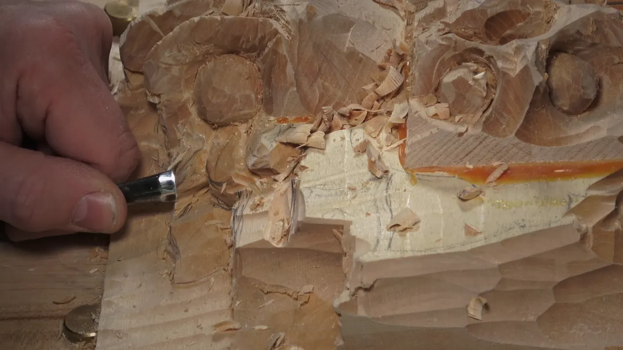 Hand with a gouge at the tall block, two round nuts beside it