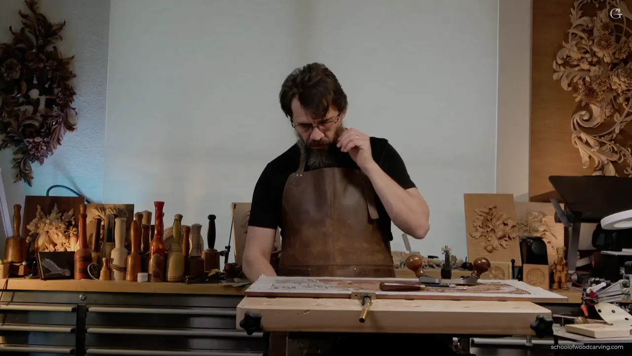 Standing in a leather apron at a wood bench with two vise handles, a row of mallets on the shelf behind