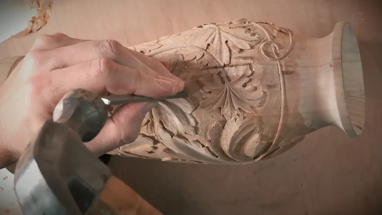 A hand holds a punch to the carved vase while a hammer comes down.