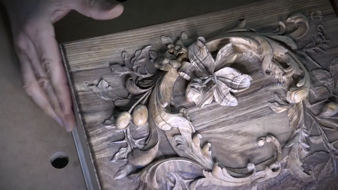 A hand rests at the edge of the colored lid, with the carved lily in the middle