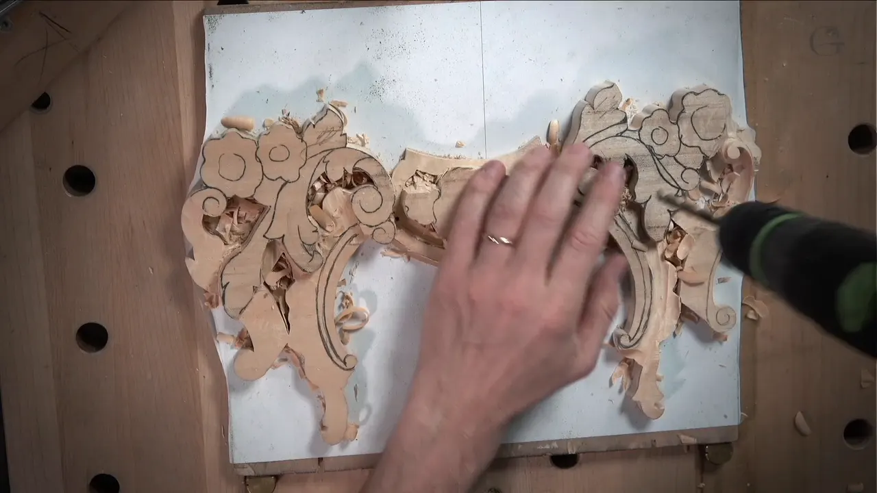 Seen from above, a cordless drill goes into the blank by the right-hand scroll while his other hand lies flat on it