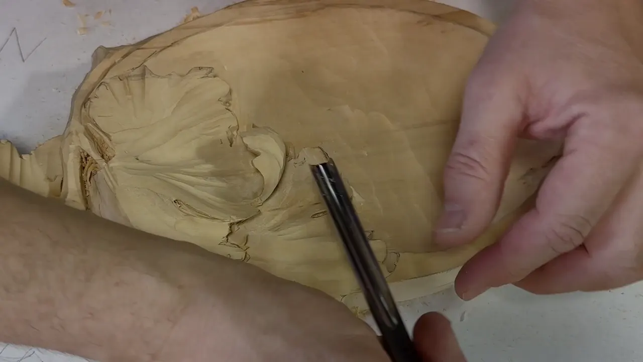 One hand steadies the tray while a gouge stands upright at the edge of a curled leaf lobe