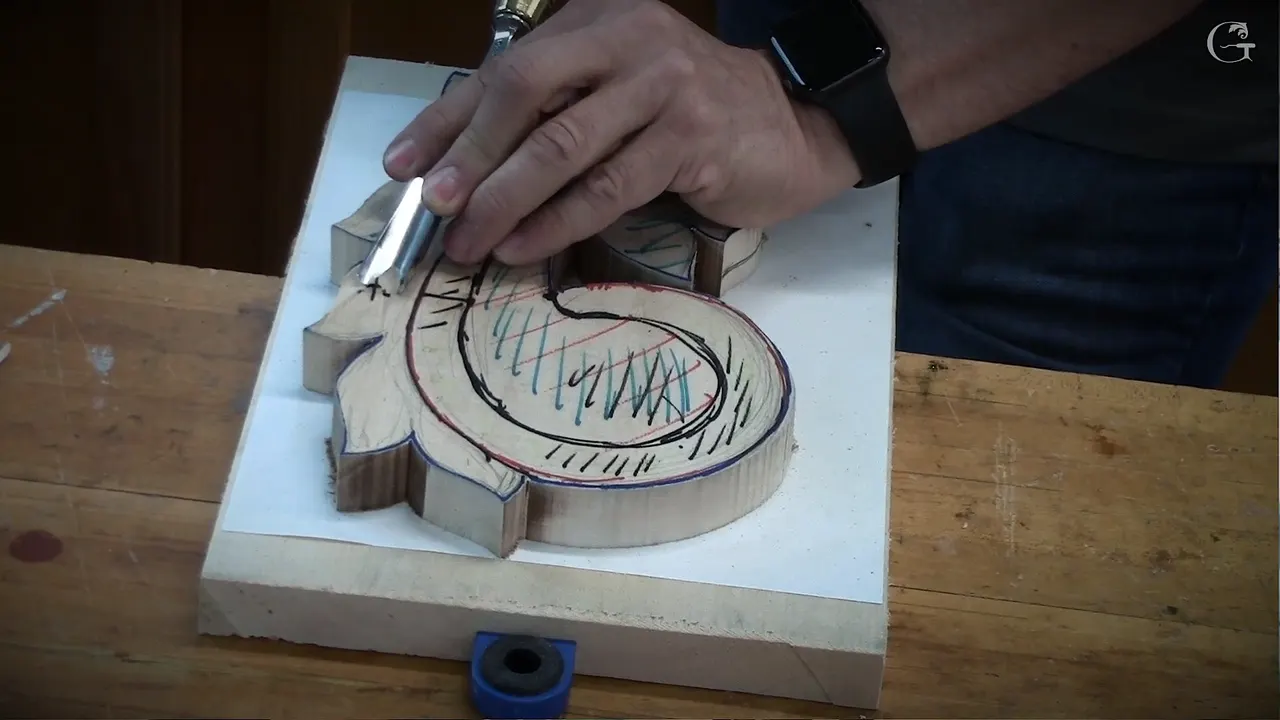 A hand grips the steel of a gouge at the edge of a carved leaf blank