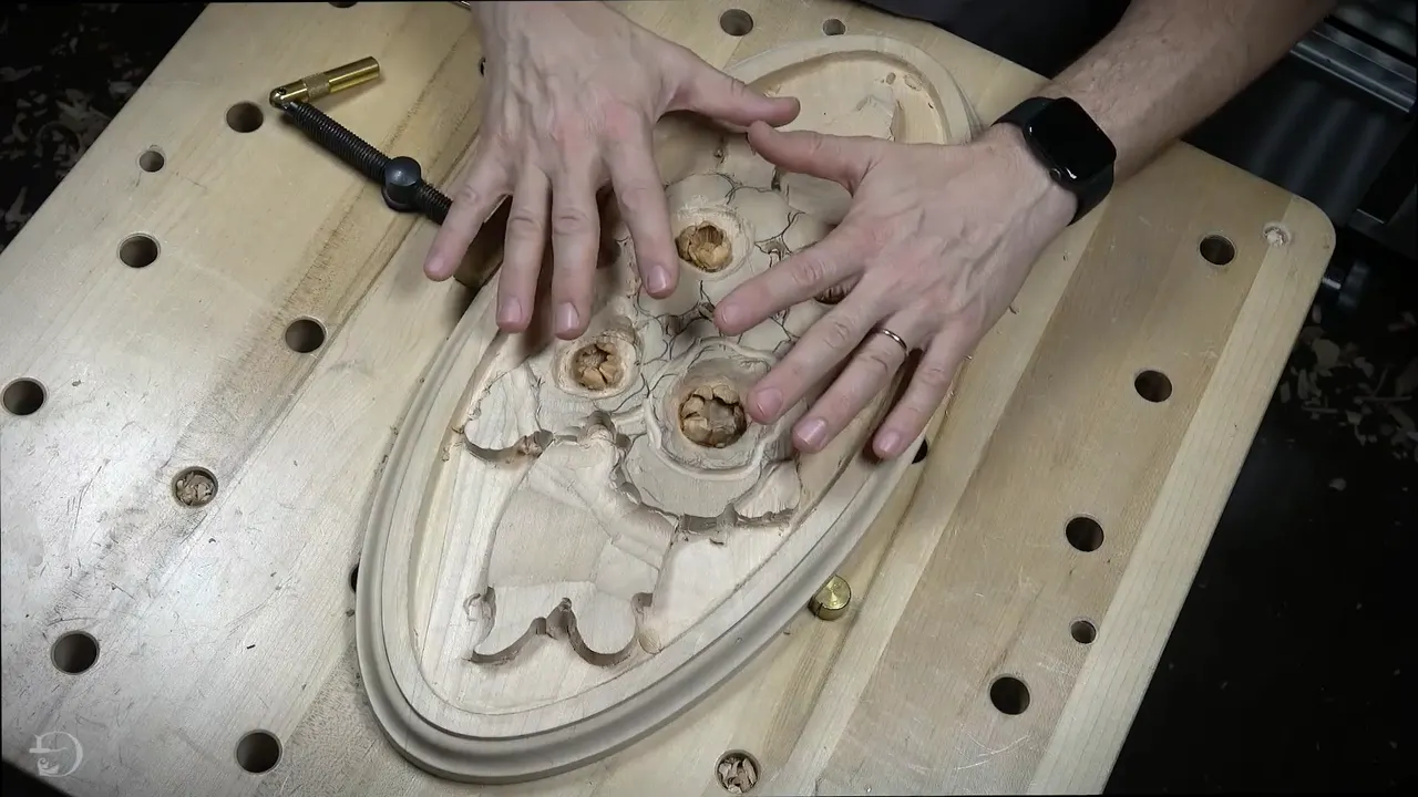 Two hands rest on an oval rosette carving with four small flowers, held on a bench full of holes