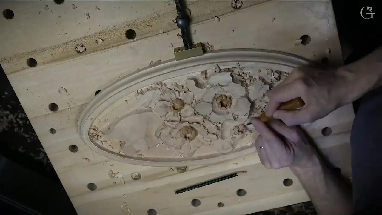 Overhead, the oval held by a metal clamp, both hands on a small tool by the flowers, a pencil below