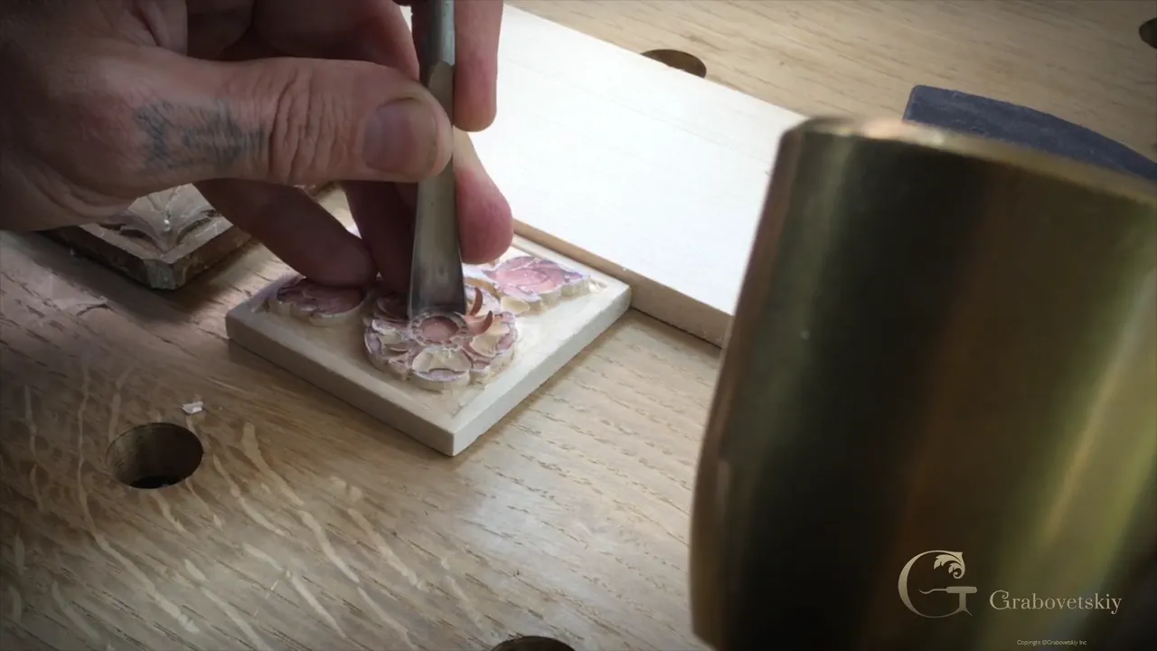 A gouge stands upright among the petals while a heavy brass mallet waits just to its right
