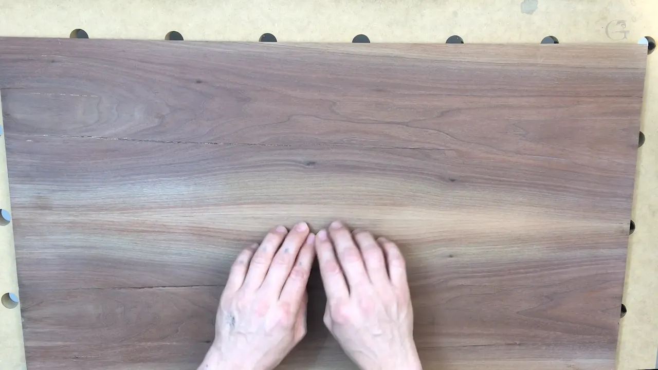 Two hands rest side by side on a wide walnut board laid over a pegboard bench.
