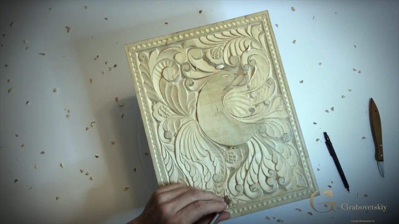 The whole carved bird panel on a white bench, a scalloped border all round it, a pencil and a knife lying beside it
