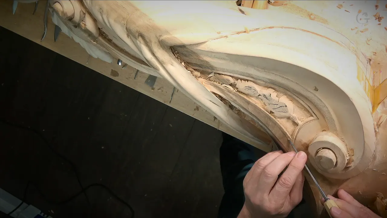 Both hands guide a slim tool along the inside curve of a carved scroll.