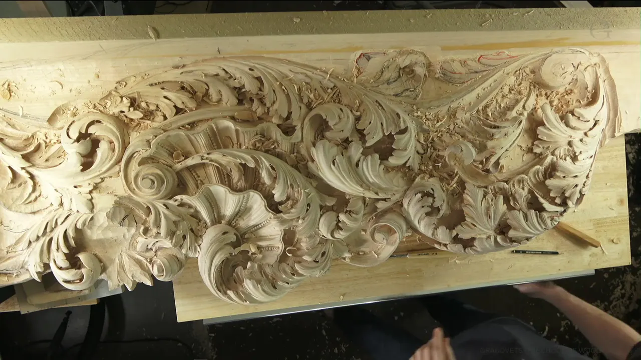 A long carved panel of leaves and scrolls seen from above, pencils lying on the bench below it